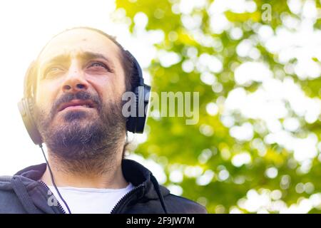 Hippy uomo con barba e cuffie per ascoltare musica all'aperto il giardino Foto Stock