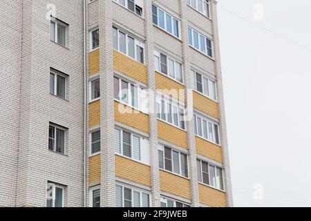 Facciata di un alto edificio con finestre in plastica e balconi. Sullo sfondo del cielo grigio. Edifici nuovi e moderni, facciate degli edifici. Concetto di architettura immobiliare e urbana. Foto Stock