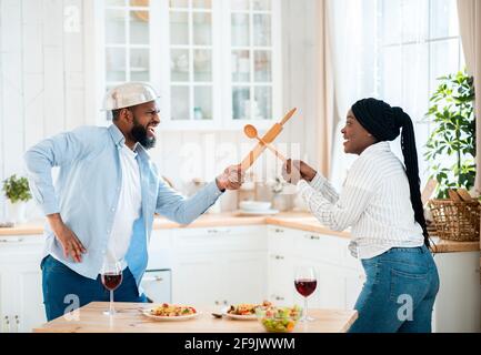 Divertente coppia nera divertirsi in cucina, utilizzando gli utensili da cucina per giocare lotta Foto Stock