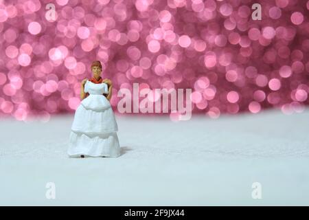 Le donne in miniatura si levano in piedi sopra la mattonella bianca provando l'abito da sposa con il bokeh sfondo rosa chiaro. Foto immagine Foto Stock