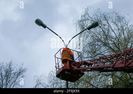 Un lavoratore municipale in un dispositivo di protezione che sostituisce le lampadine di una lampada da strada. Un lavoratore che ripara una lampada di strada di un elevatore di secchio. Foto Stock