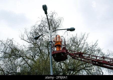 Un lavoratore municipale in un dispositivo di protezione che sostituisce le lampadine di una lampada da strada. Un lavoratore che ripara una lampada di strada di un elevatore di secchio. Foto Stock