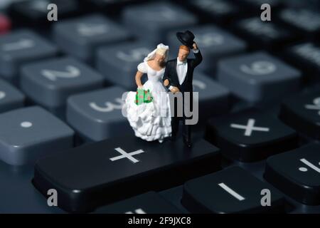 Le persone in miniatura di sposo e sposa si trovano sopra la calcolatrice. Piano di nozze bilancio e concetto finanziario Foto Stock