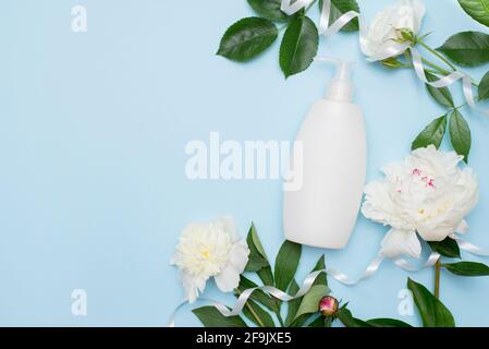 fiori bianchi e shampoo o gel doccia su sfondo blu. Beauty concetto femminile. Disposizione piatta, spazio di copia Foto Stock