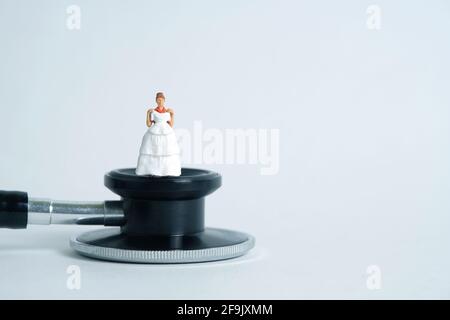 Matrimonio matrimonio matrimonio e coppia medica check-up concetto miniatura persone giocattolo fotografia. Sposa e sposo con stetoscopio isolato su sfondo bianco. Foto Stock
