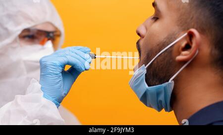 Primo piano del campione per il prelievo del test di positività COVID-19. Personale medico in tuta protettiva con tampone per prelevare il campione dalla bocca maschile. Foto Stock