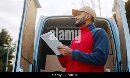 Vista dal basso angolo della vita di un professionista logistico utilizzando un tablet digitale. Aprire le porte posteriori del furgone con i pacchi sullo sfondo. Foto Stock