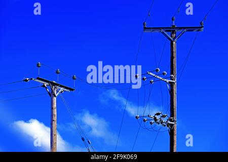 Poli telefonici cavi di linea e di alimentazione contro il cielo blu profondo Foto Stock