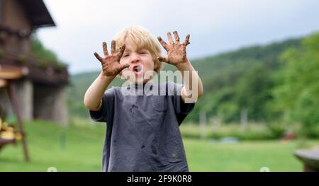 Piccolo ragazzo con mani sporche in piedi in orto, stile di vita sostenibile. Foto Stock