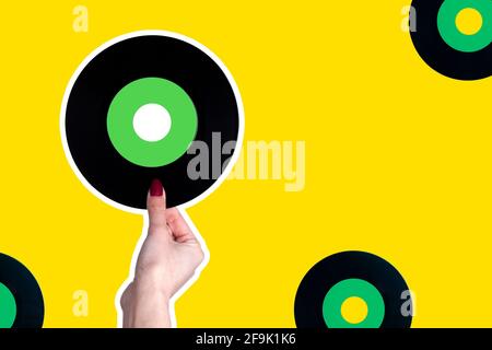 la mano femmina contiene un disco in vinile da 45 giri/min. Isolare su sfondo giallo. Concetto di pop Foto Stock