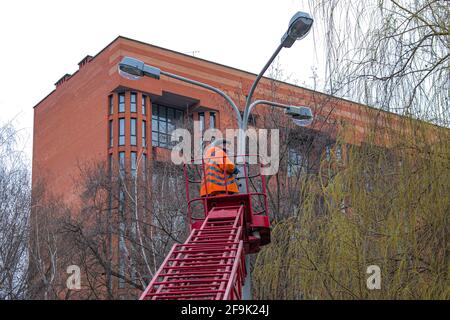 Dnepropetrovsk, Ucraina - 04.12.2021: Un operaio comunale in dispositivi di protezione che sostituisce le lampadine in una lampada da strada. Un lavoratore che ripara una lampada di strada di un bu Foto Stock