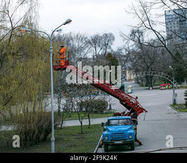 Dnepropetrovsk, Ucraina - 04.12.2021: Un operaio comunale in dispositivi di protezione che sostituisce le lampadine in una lampada da strada. Un lavoratore che ripara una lampada di strada di un bu Foto Stock