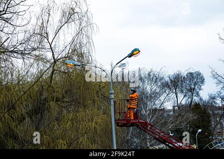 Dnepropetrovsk, Ucraina - 04.12.2021: Un operaio comunale in dispositivi di protezione che sostituisce le lampadine in una lampada da strada. Un lavoratore che ripara una lampada di strada di un bu Foto Stock