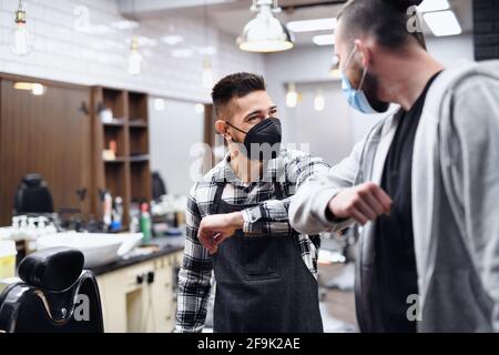 Uomo saluto haidresser con gomito a gomito in barbiere, coronavirus e nuovo concetto normale. Foto Stock