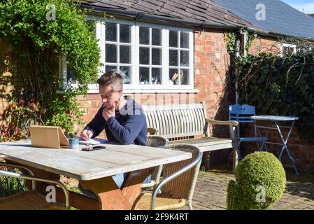 Uomo che lavora da casa a distanza lavorando online in giardino Foto Stock