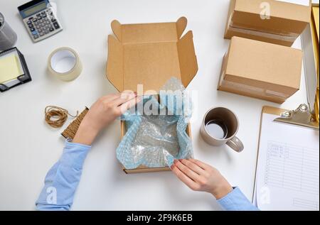consegna la tazza di imballaggio alla scatola del pacco presso l'ufficio postale Foto Stock