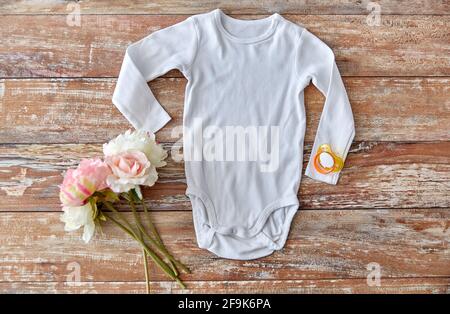 bodysuit bambino con succhietto e fiori su legno Foto Stock