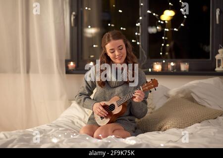 felice giovane donna che suona la chitarra a letto a casa Foto Stock