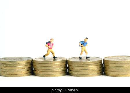 Budget di ingresso alla scuola. Bambini o bambini, camminando sopra la pila di moneta d'oro. Fotographia dei giocattoli della gente piccola in miniatura. Isolato su backgroun bianco Foto Stock