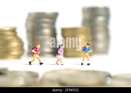 Budget di ingresso alla scuola. Bambini o bambini, camminando tra le pile di moneta. Fotographia dei giocattoli delle piccole persone in miniatura. Isolato su sfondo bianco. Foto Stock