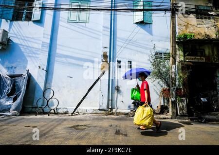 Una donna che tiene un ombrello blu cammina davanti a un edificio di colore blu chiaro a Bangkok, Thailandia. Foto Stock