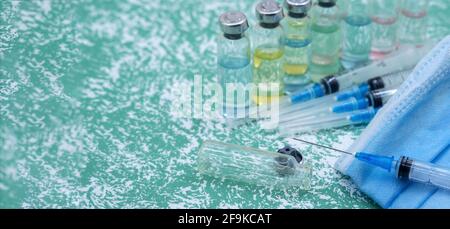 Prevenzione delle malattie stagionali. Fiale mediche, siringhe e una maschera su sfondo verde. Vaccinazione contro covid-19. Foto Stock