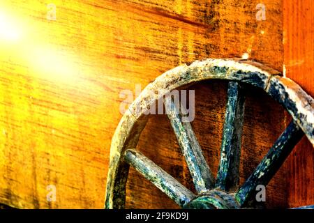 Primo piano di età ruota di carro con raggi di legno appoggiati contro una scatola di legno gialla, astratta Foto Stock