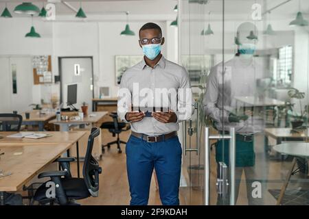 Uomo d'affari africano che indossa una maschera facciale che lavora su un tablet Foto Stock