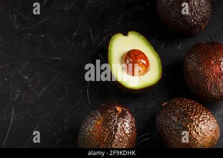 Avocado di Hass affettato maturo con osso su sfondo nero testurizzato. Vista dall'alto, spazio libero Foto Stock