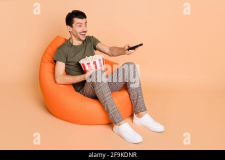 Foto di profilo a dimensione intera di un brunetto impressionato ragazzo sit orologio sneakers t-shirt da tv isolate su sfondo di colore beige Foto Stock