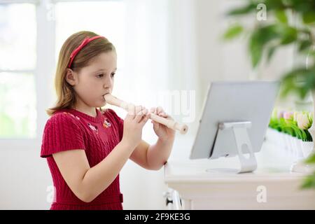 Bambino che gioca flauto. Apprendimento remoto da casa. Arti per bambini. Bambina con strumento musicale. Lezione di videoconferenza. Foto Stock