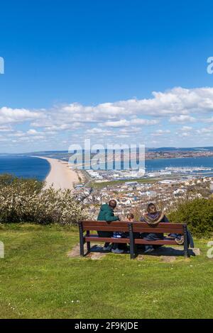 La famiglia in panchina gode di vedute della spiaggia di Chesil Bank e di Fortuneswell, Isola di Portland da Portland Heights, Portland, Weymouth Dorset, Regno Unito ad aprile Foto Stock