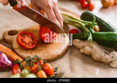 tritare a mano il pomodoro sul legno preparare il pranzo primaverile con verdure fresche come melanzane e carote su tessuto rustico. concetto di cibo primaverile e organo Foto Stock