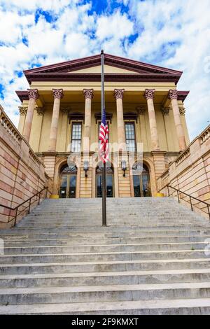 Lancaster, PA, USA - 18 aprile 2021: La bandiera degli Stati Uniti vola a metà albero all'ingresso della parte più vecchia del tribunale della contea di Lancaster a Lancaster Foto Stock