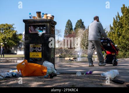 Pinner Regno Unito. Aprile 2021. Traboccante bidone dei rifiuti presso il ducklaghetto presso il Memorial Park, Pinner, Middlesex, Regno Unito. L'uomo cammina oltre spingendo pRAM. Foto Stock