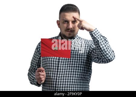 Un ragazzo bianco che tiene una bandiera del Marocco e un dito tocca il tempio sulla testa isolato su uno sfondo bianco. Foto Stock