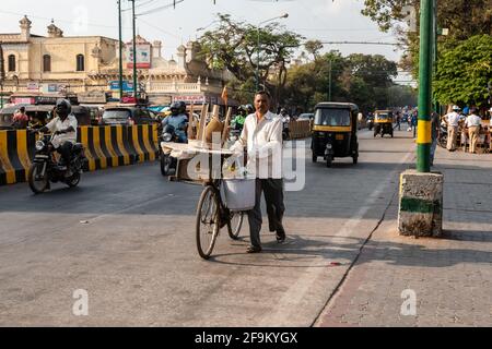 Mysuru, Karnataka, India - Gennaio 2019: Un venditore di strada che cammina con la sua bicicletta su una strada trafficata nella città di Mysore. Foto Stock