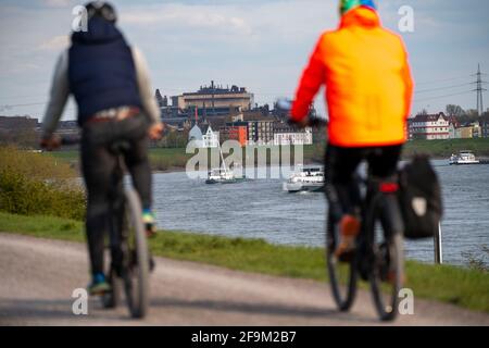 Ciclisti sulla diga del Reno, navi da carico sul Reno vicino Duisburg-Laar, case sulla strada della diga, scenario industriale della ArcelorMittal Hochfeld GM Foto Stock