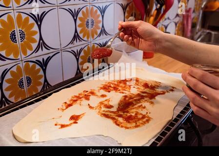 Versare un cucchiaio di pomodoro fritto sulla base di un impasto per preparare una pizza Foto Stock