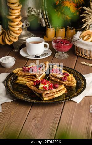 Ancora vita con tradizionali ucraini e frittelle russe per il Maslenitsa vacanza con burro e bacche su un vassoio nero con un samovar Foto Stock