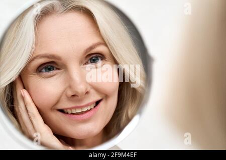 Felice donna di mezza età che guarda lo specchio. Concetto di cura di bellezza anti-aging. Foto Stock