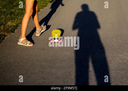 Defocalizzare il bambino con il penny skateboard sul sentiero nel parco. Il ragazzo e la ragazza cavalcano una tavola di penny nel giorno del sole. Foto stile di vita all'aperto su una somma di sole Foto Stock