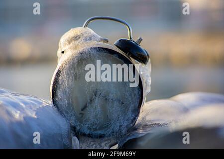 Orologio congelato sveglia in ghiaccio sulla spiaggia tra due rocce. Foto Stock