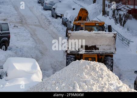 trattore che rimuove la neve dal parcheggio vicino a un edificio residenziale durante la giornata invernale Foto Stock