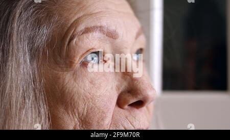 Primo piano ritratto di donna anziana triste con occhi blu capelli grigi e pelle rugosa. Foto di alta qualità Foto Stock