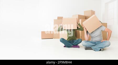 Giovane con scatole sulle loro teste seduto sul pavimento nella loro nuova casa, sensazione sottolineato Foto Stock