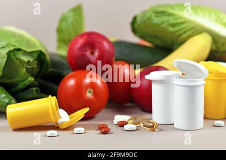 Bottiglie con pillole di integratori alimentari di fronte frutta e verdura sullo sfondo Foto Stock