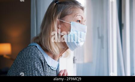 Ritratto di donna anziana con maschera medica in quarantena guardando attraverso la finestra. Foto di alta qualità Foto Stock