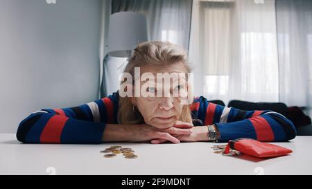 Anziana pensionato disperata che guarda una piccola quantità di monete sul tavolo. Foto di alta qualità Foto Stock