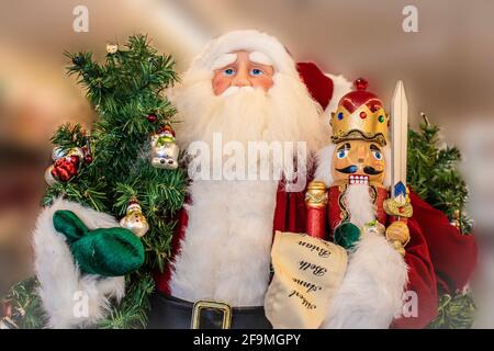 Decorazione artificiale Babbo Natale figura che tiene un albero e un nutcracker e una lista di buoni ragazzi e ragazze contro sfondo sfocato - vita in su Foto Stock